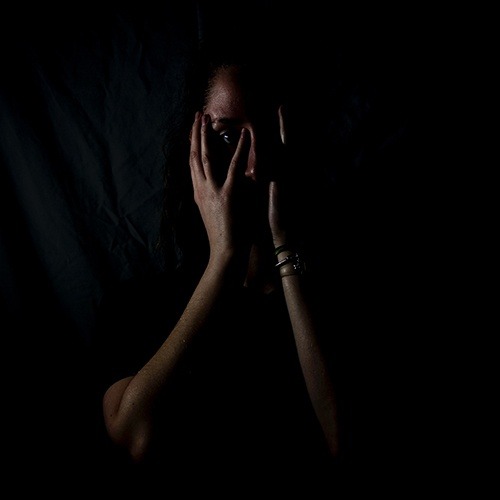 Girl covering her face in a dark background.